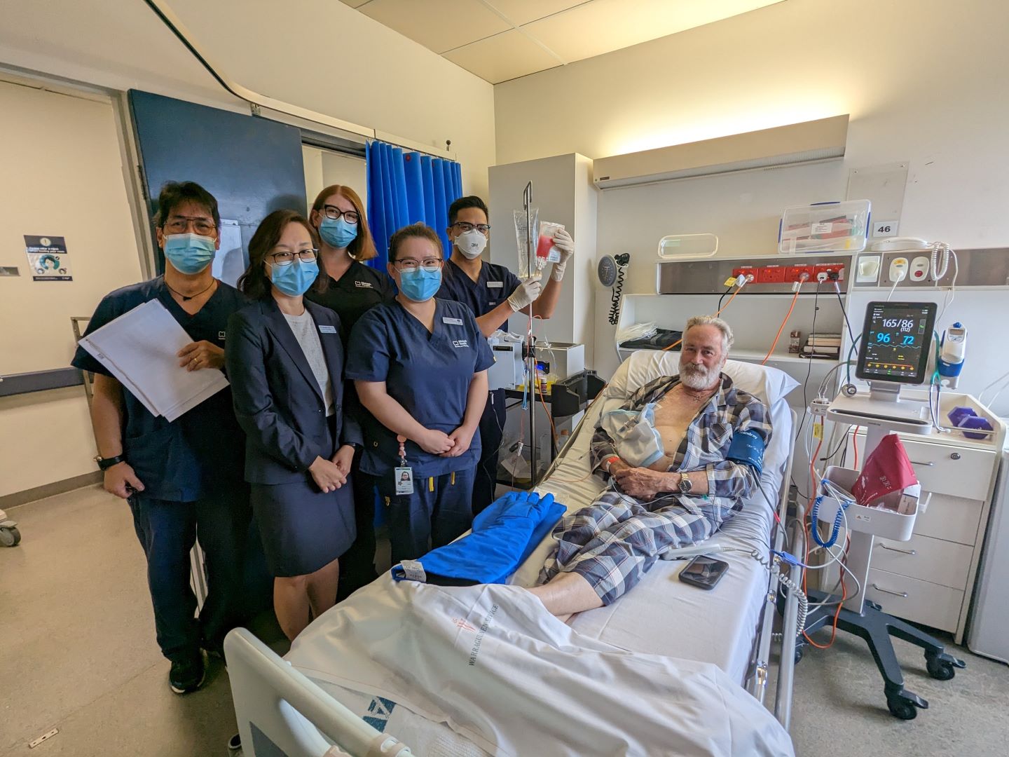 Dr Danielle Oh and her medical team pose next to Phillip Mawdsley, who is a patient on a hospital bed.