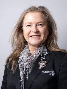 A lady with medium-length blonde hair wearing a blazer, smiling to camera