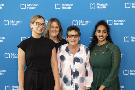 Four ladies smile to camera, standing in front of a blue Monash Health media wall