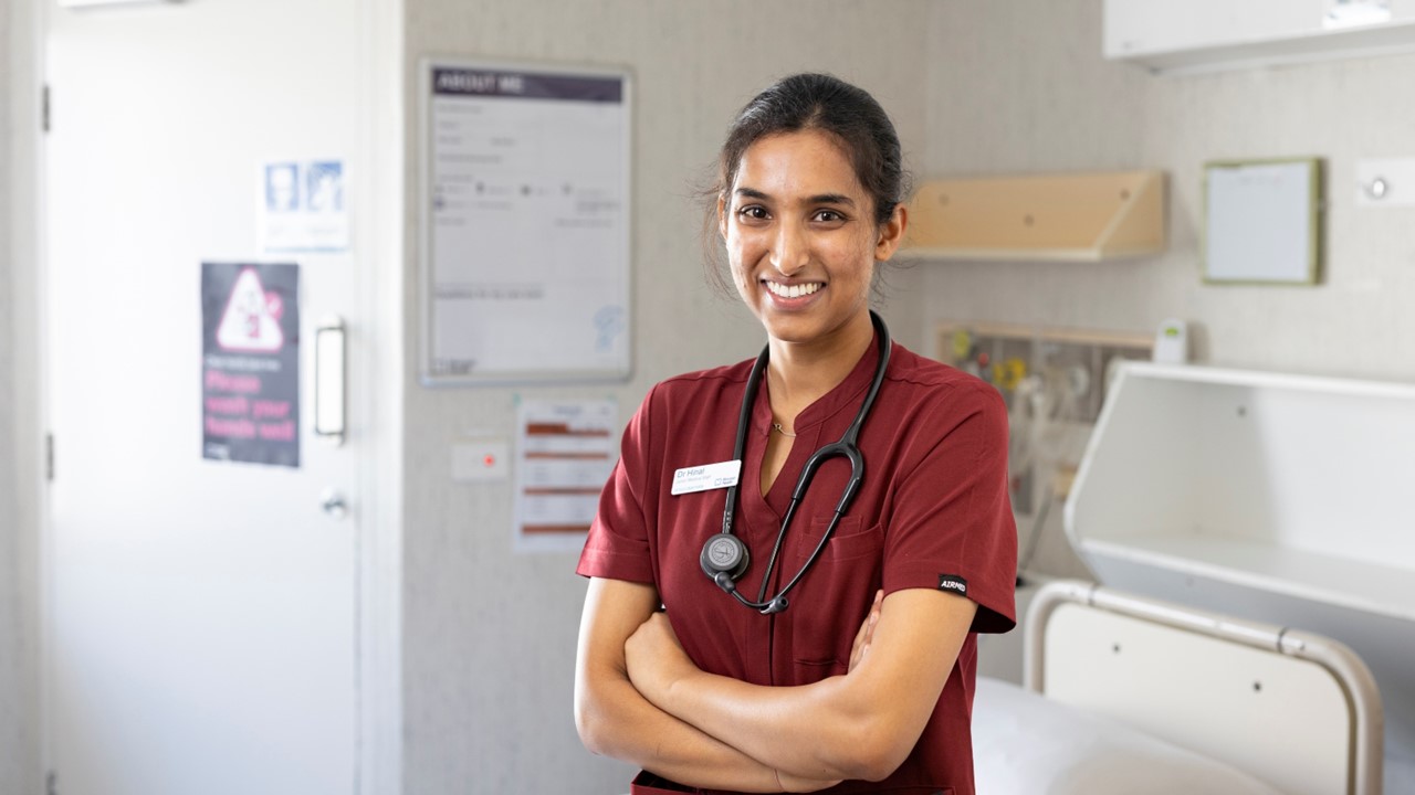 A woman wearing scrubs standing in front of a hospital bed